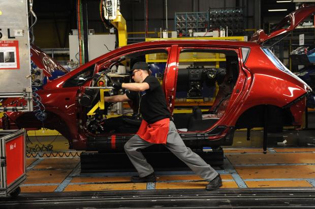 Worker installing a dashboard in a red Nissan Leaf on a car assembly line.