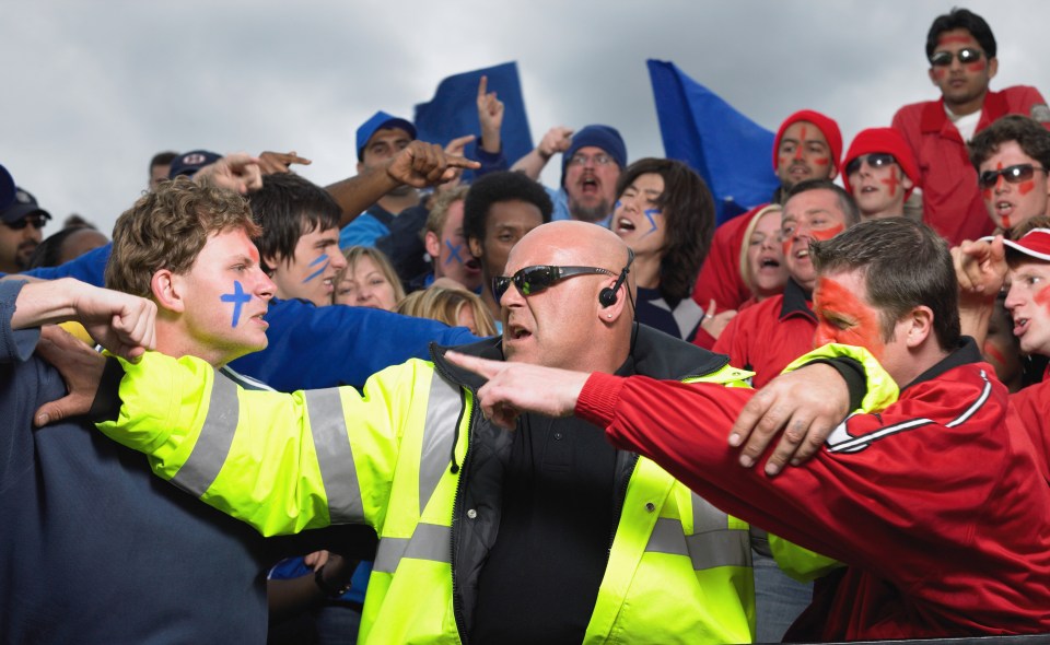 Security guard breaking up a fight between two fans at a sporting event.