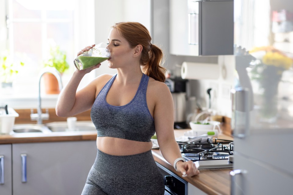 Woman in sportswear drinking a green smoothie in her kitchen.