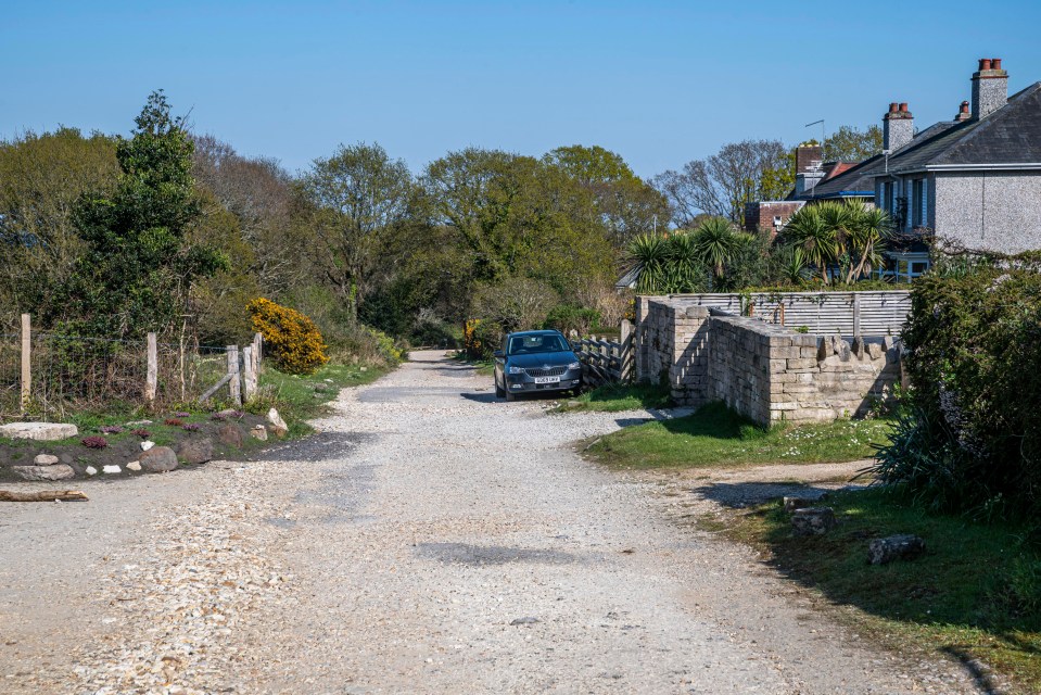 A car parked on a gravel road in front of houses.