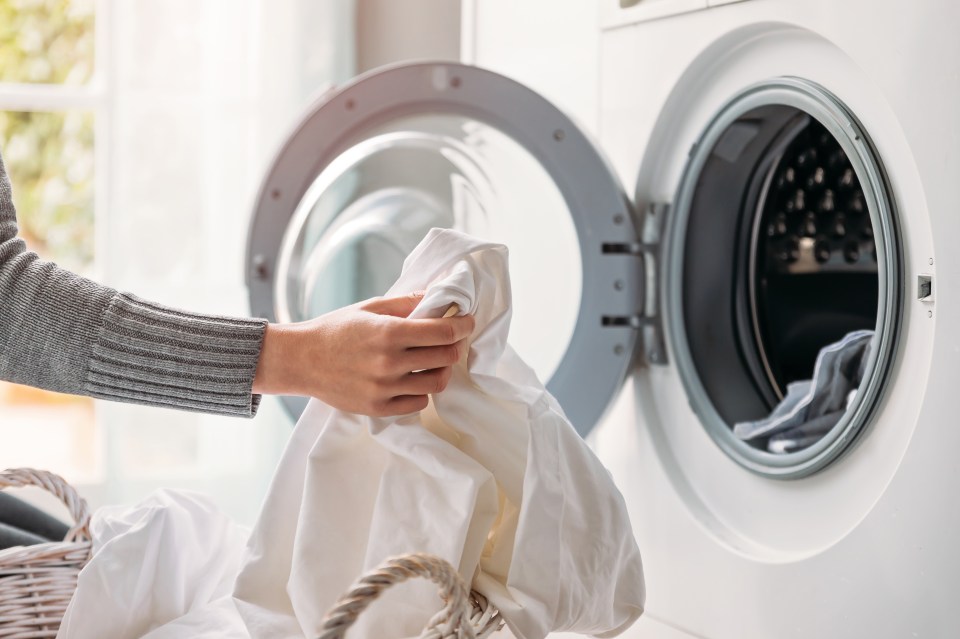 Woman's hands putting white laundry into a washing machine.