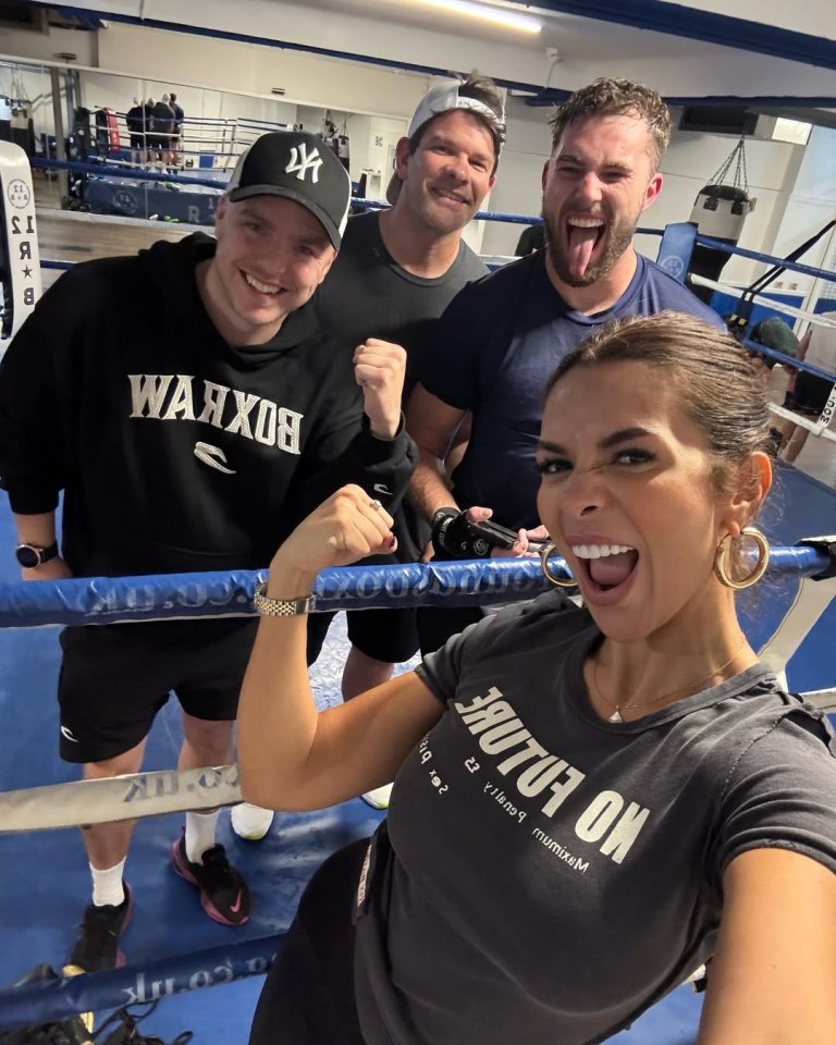 Four people in a boxing gym, one flexing their bicep.