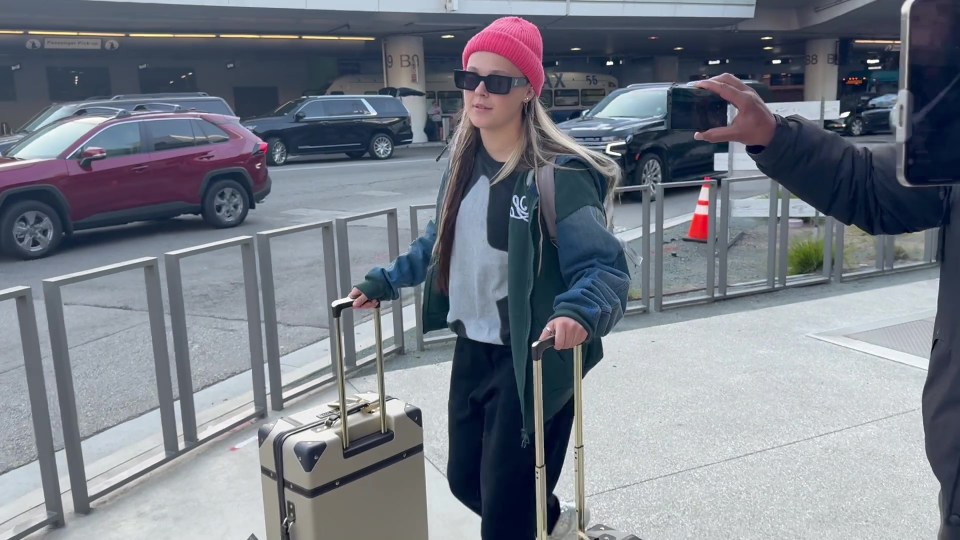 JoJo Siwa at an airport, pulling two suitcases.