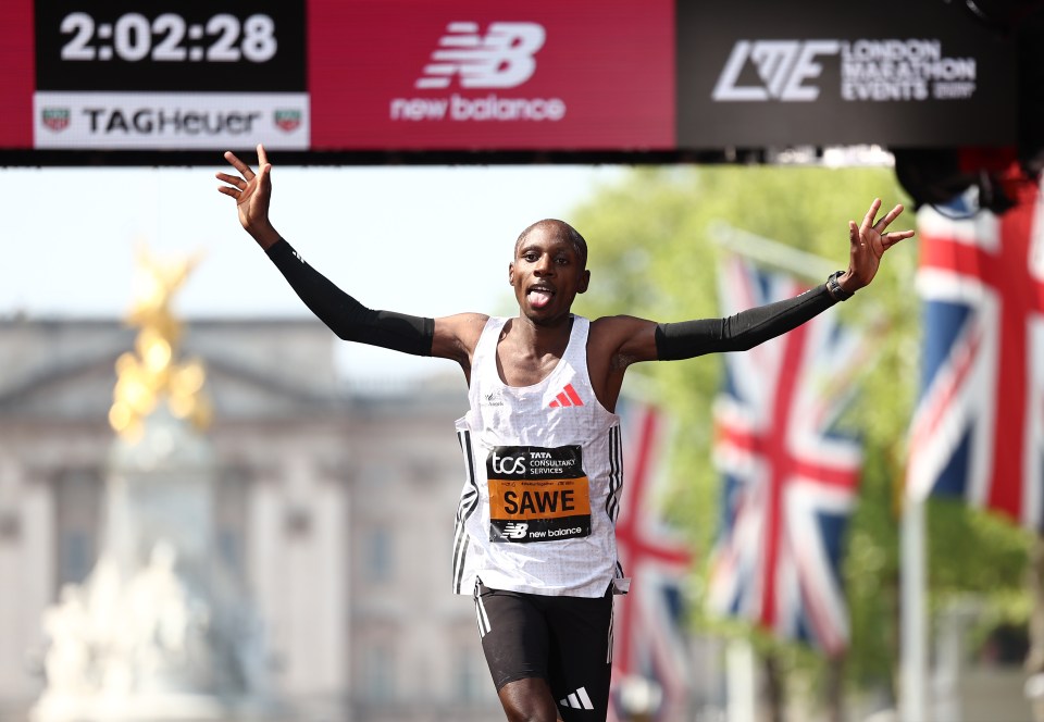 Marathon runner Sabastian Sawe crossing the finish line with arms raised.