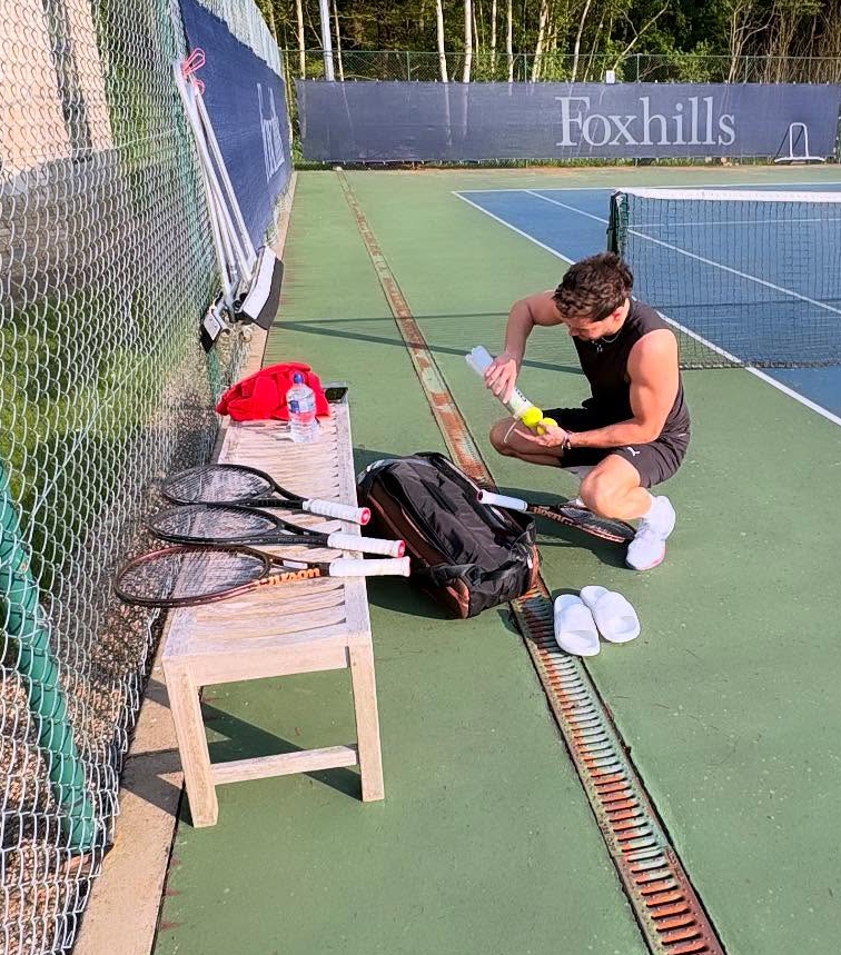 Man preparing tennis equipment on a court.