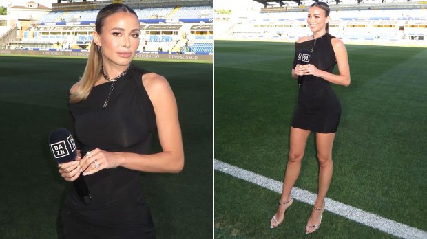 A woman in a black dress holds a DAZN microphone in front of a soccer field.