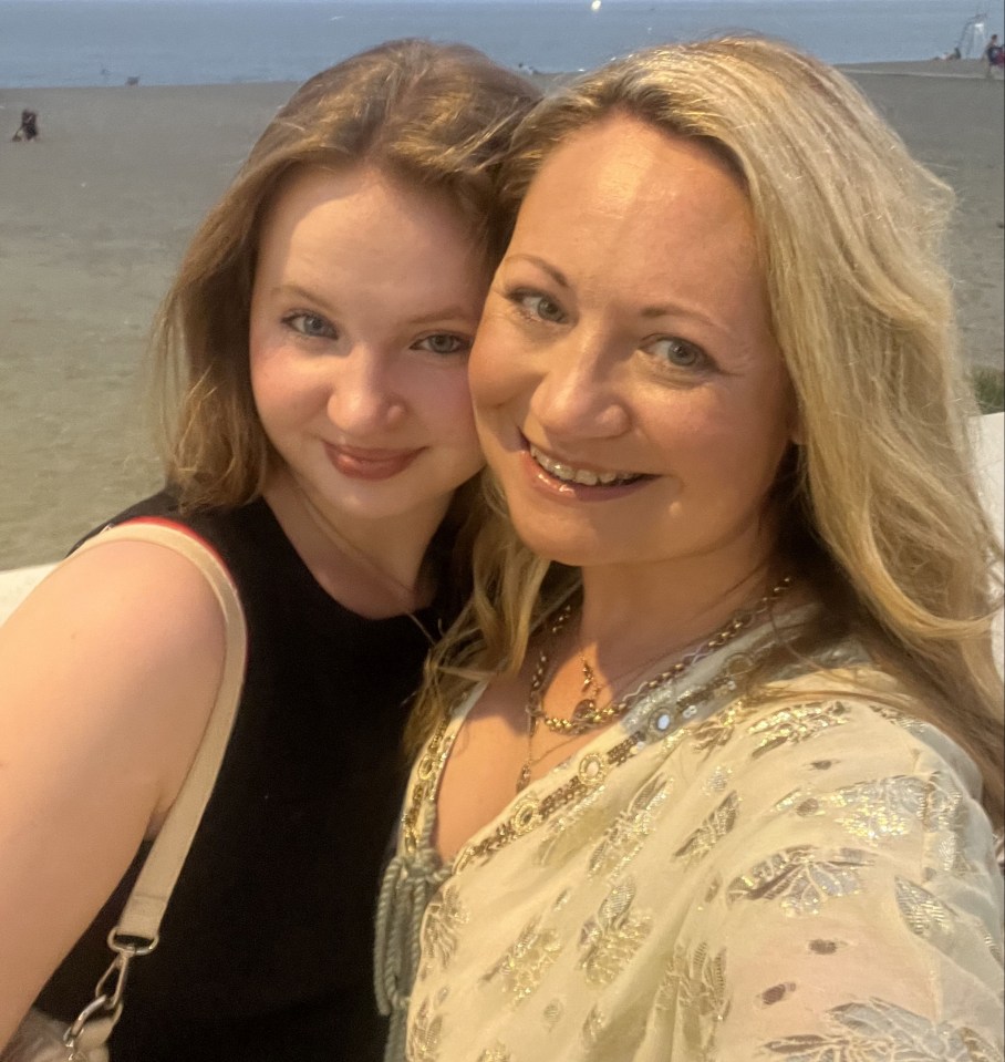 A mother and daughter pose for a photo on a beach.
