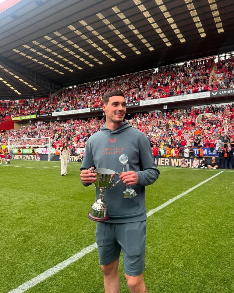 Footballer Lloyd Jones holding two trophies on a football pitch.