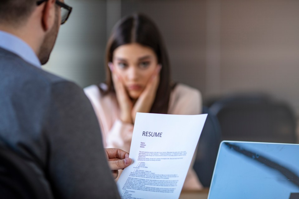 A nervous job applicant sits across from an interviewer who is reviewing her resume.