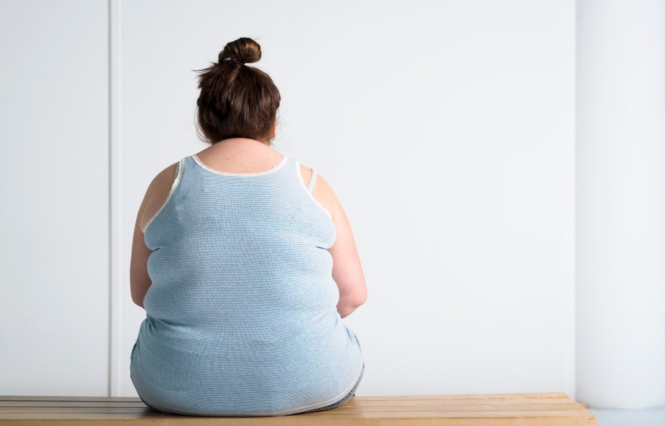 Overweight teenage girl sitting on a bench, viewed from behind.