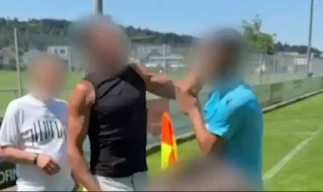 Blurred photo of three people on a soccer field, one appearing to restrain another.